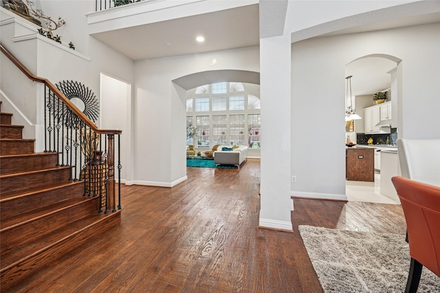 entryway with a towering ceiling, arched walkways, wood finished floors, stairway, and recessed lighting