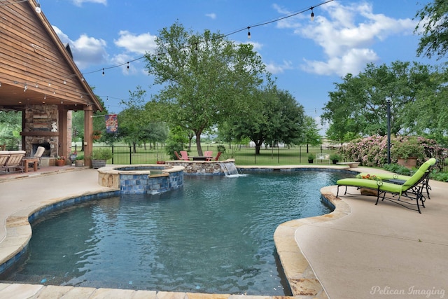 view of swimming pool with an outdoor stone fireplace, a pool with connected hot tub, fence, and a patio area