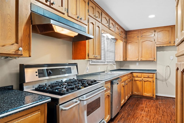 kitchen with brown cabinetry, dark wood-type flooring, under cabinet range hood, a sink, and stainless steel appliances