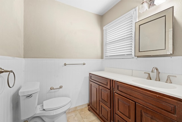bathroom with vanity, toilet, tile patterned floors, and a wainscoted wall
