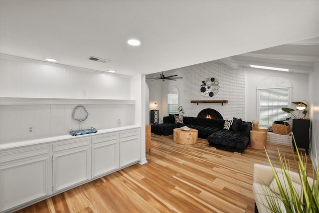 living area with ceiling fan, a fireplace, vaulted ceiling, light wood-type flooring, and visible vents