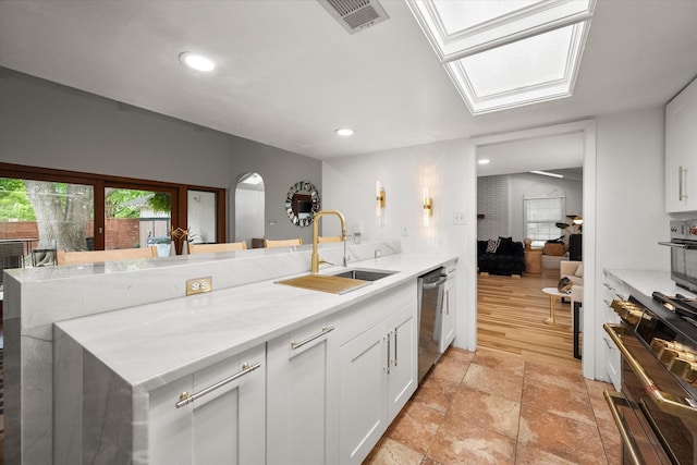 kitchen with a sink, dishwasher, arched walkways, white cabinetry, and visible vents