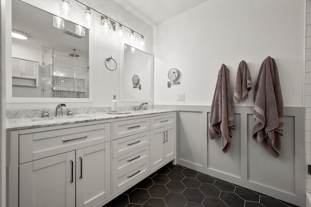 full bath featuring double vanity, tile patterned flooring, a tile shower, wainscoting, and a sink