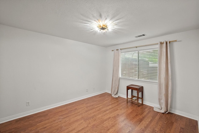 spare room featuring baseboards, light wood-type flooring, a textured ceiling, and visible vents