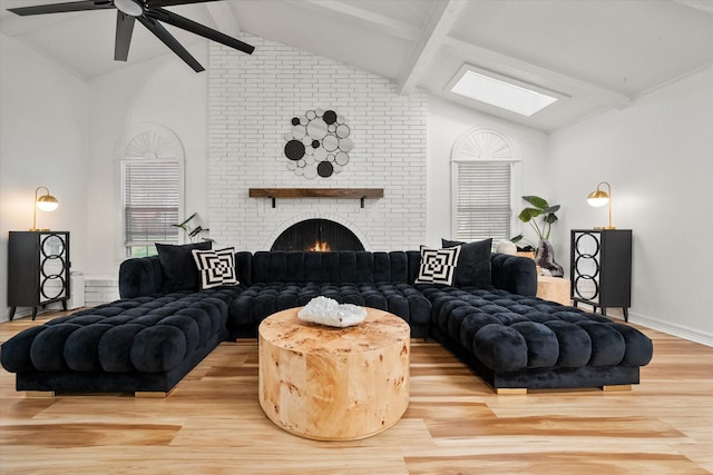 living room featuring ceiling fan, a brick fireplace, lofted ceiling with skylight, and wood finished floors