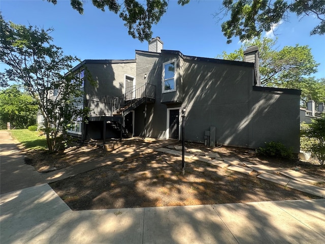 view of front of property with a deck, stairs, a chimney, and stucco siding