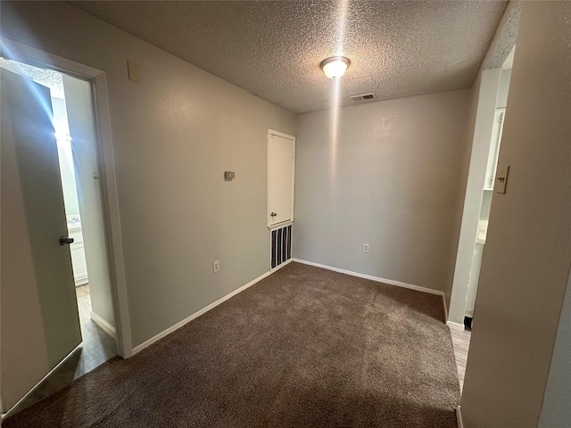spare room with a textured ceiling, visible vents, baseboards, and dark colored carpet