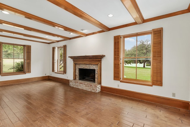 unfurnished living room with plenty of natural light, a fireplace with raised hearth, beam ceiling, and wood finished floors
