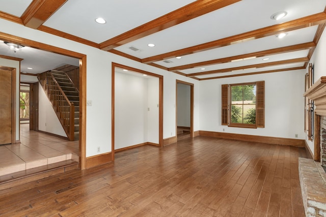 unfurnished living room with a fireplace with raised hearth, a healthy amount of sunlight, hardwood / wood-style flooring, and beamed ceiling