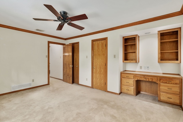 unfurnished office with light carpet, a ceiling fan, built in desk, and visible vents