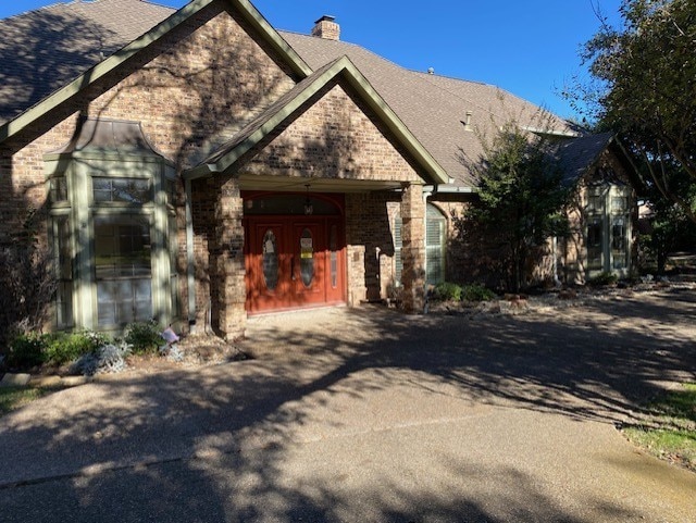 view of front of property featuring brick siding, a chimney, roof with shingles, and aphalt driveway