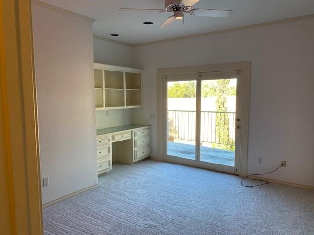 unfurnished office with ornamental molding, baseboards, light colored carpet, built in desk, and a ceiling fan