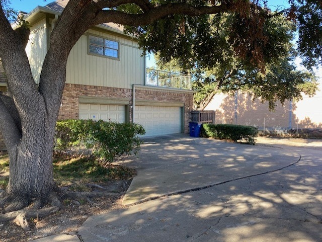 view of front of property featuring a balcony, a garage, driveway, and brick siding