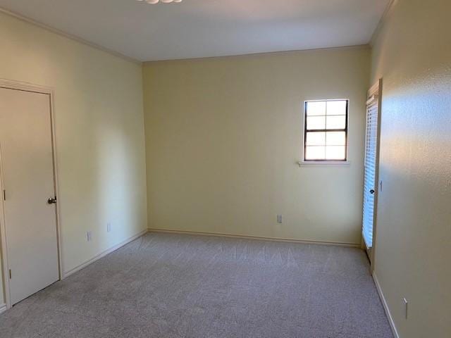 empty room featuring light colored carpet, ornamental molding, and baseboards