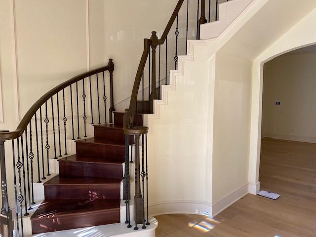 stairway featuring arched walkways, baseboards, and wood finished floors