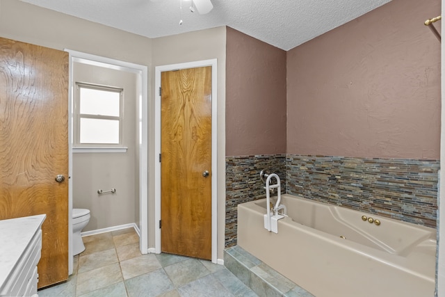 full bath featuring ceiling fan, vanity, toilet, a textured ceiling, and a garden tub