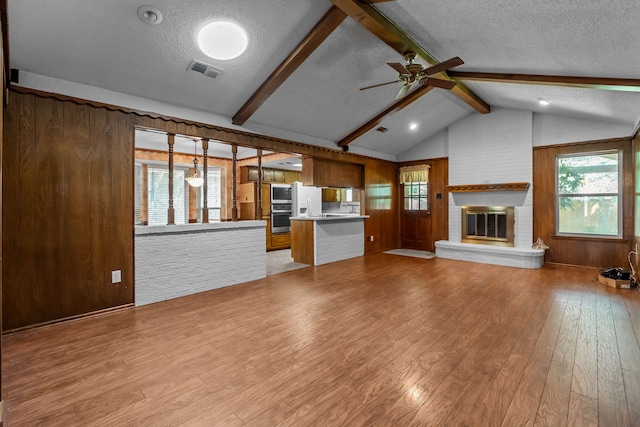 unfurnished living room with visible vents, a textured ceiling, ceiling fan, and wooden walls