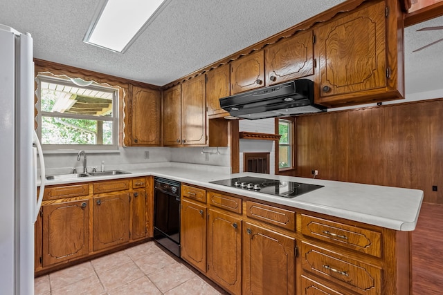 kitchen featuring a sink, a textured ceiling, brown cabinetry, under cabinet range hood, and black appliances