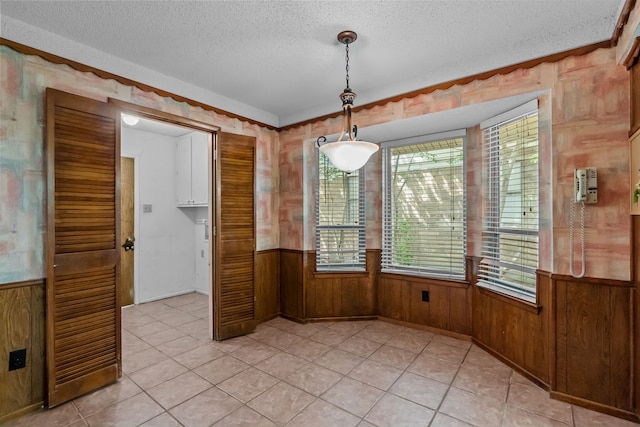 unfurnished dining area featuring wood walls, a textured ceiling, light tile patterned floors, and a wainscoted wall