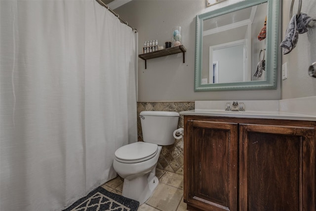 full bathroom with toilet, a wainscoted wall, tile walls, tile patterned flooring, and vanity
