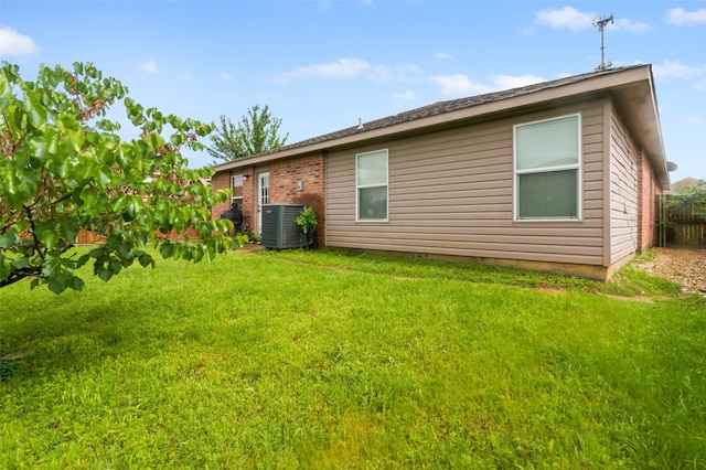 rear view of property with brick siding, fence, central AC, and a lawn