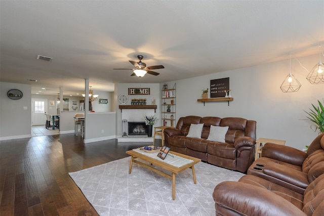 living area with a ceiling fan, a fireplace with raised hearth, baseboards, visible vents, and wood finished floors