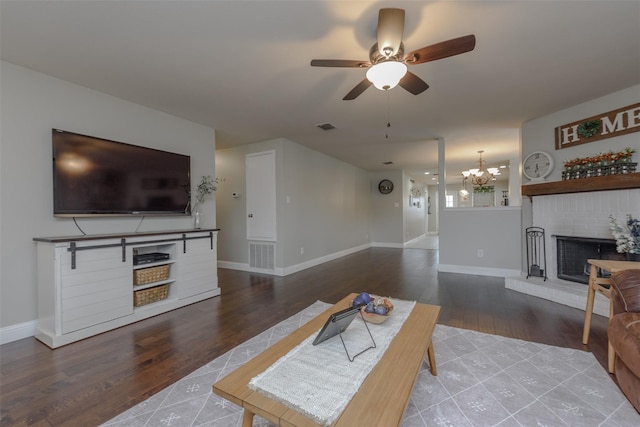 living area featuring a brick fireplace, ceiling fan with notable chandelier, visible vents, and wood finished floors