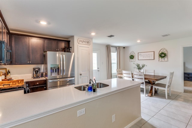 kitchen with dark brown cabinetry, visible vents, black microwave, a sink, and stainless steel fridge