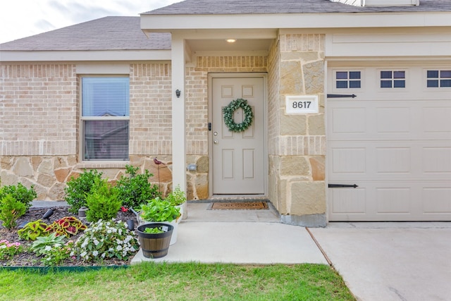 entrance to property with brick siding, an attached garage, stone siding, and roof with shingles