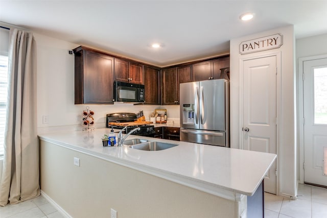 kitchen featuring light tile patterned flooring, black microwave, stainless steel fridge, a sink, and range