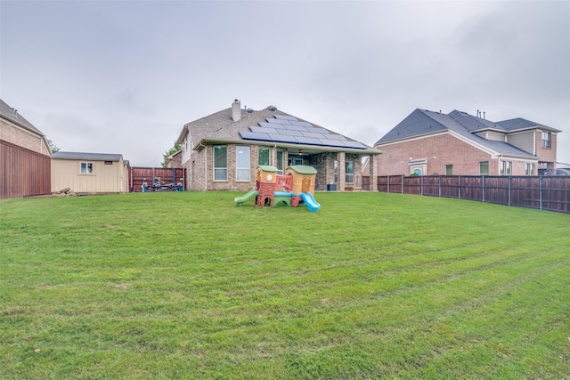 back of property featuring a playground, a yard, a fenced backyard, and brick siding