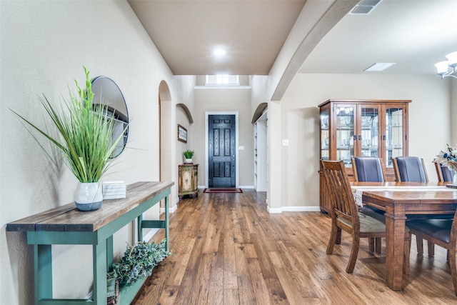 entryway with arched walkways, baseboards, visible vents, and wood finished floors