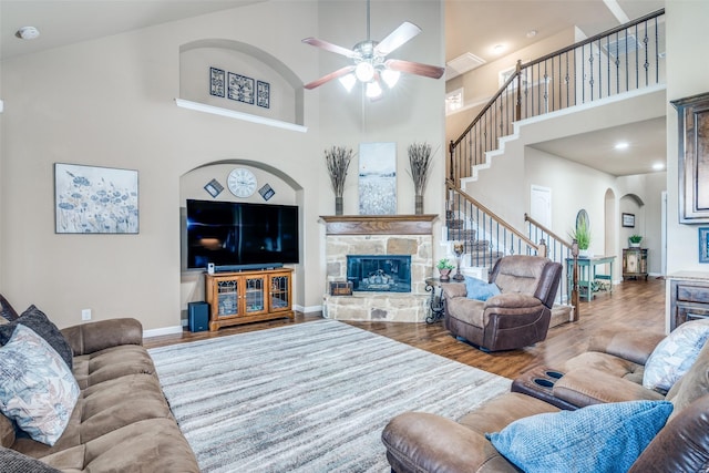 living room featuring ceiling fan, a towering ceiling, arched walkways, a fireplace, and stairway