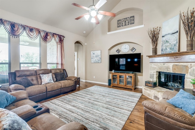living room featuring a ceiling fan, wood finished floors, baseboards, high vaulted ceiling, and arched walkways