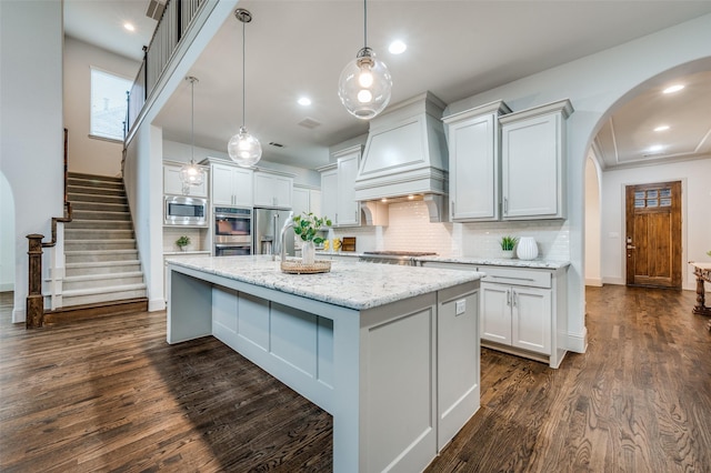 kitchen with dark wood-type flooring, custom range hood, arched walkways, backsplash, and stainless steel appliances