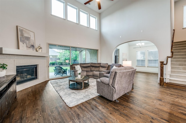 living room featuring a towering ceiling, arched walkways, wood finished floors, stairway, and ceiling fan with notable chandelier