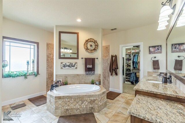 bathroom with a walk in closet, vanity, baseboards, visible vents, and a bath