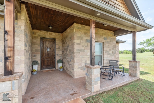 entrance to property featuring covered porch, a yard, and stone siding