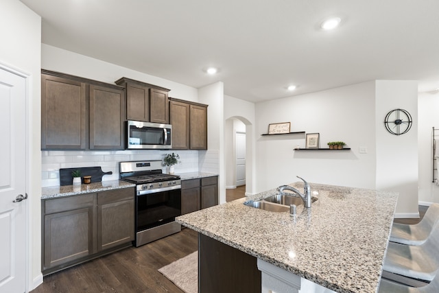 604 Stampede Ln, Princeton, TX 75407 - kitchen featuring stainless steel appliances, a sink, arched walkways, dark wood-type flooring, and decorative backsplash