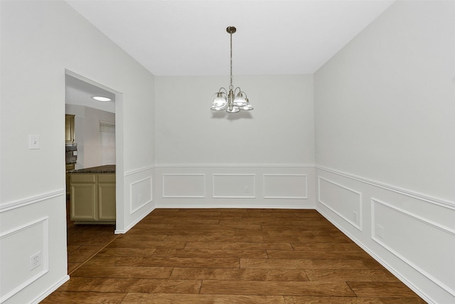 unfurnished dining area with a decorative wall, a chandelier, dark wood-style floors, and a wainscoted wall