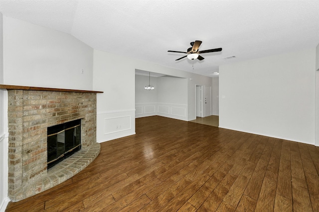 unfurnished living room with visible vents, a fireplace, wood finished floors, a wainscoted wall, and ceiling fan with notable chandelier
