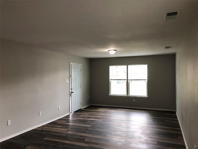 spare room featuring baseboards, dark wood-style flooring, and visible vents