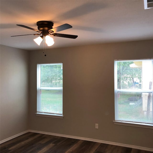empty room featuring a ceiling fan, baseboards, dark wood-style floors, and a wealth of natural light