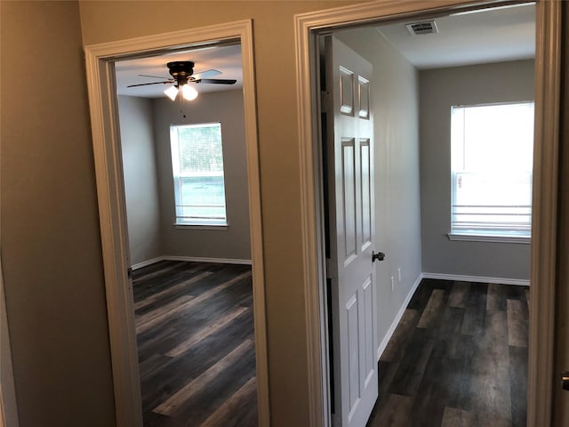 corridor with dark wood-style flooring, baseboards, and visible vents