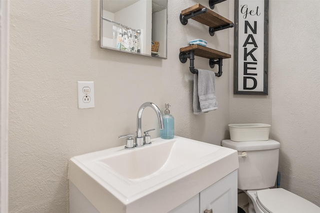 bathroom featuring toilet, a textured wall, and vanity
