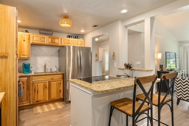 kitchen featuring freestanding refrigerator, black stovetop, a sink, and light wood-style floors