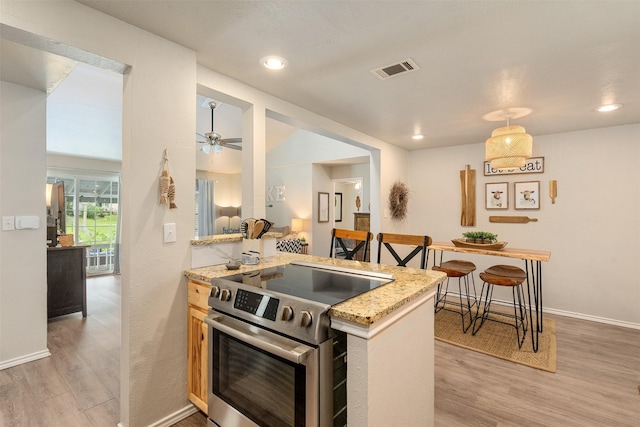 kitchen with ceiling fan, light stone counters, stainless steel range with electric stovetop, light wood-type flooring, and visible vents