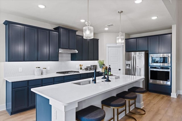 kitchen featuring appliances with stainless steel finishes, a sink, a kitchen breakfast bar, light wood-style flooring, and backsplash
