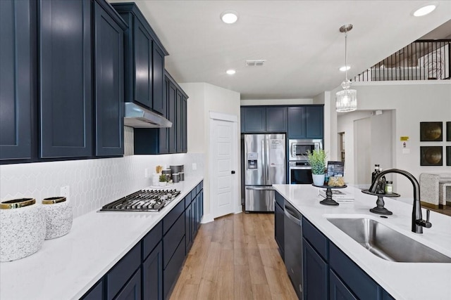 kitchen with a sink, light countertops, stainless steel appliances, tasteful backsplash, and under cabinet range hood