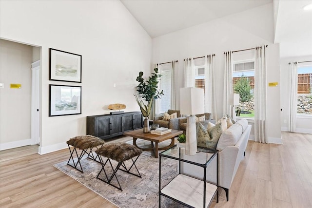 living area with high vaulted ceiling, baseboards, and light wood finished floors